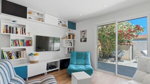 A modern living room with a flat-screen TV, bookshelves, a sofa, and a sliding glass door to the outside.