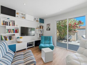 Un salon moderne doté d’un téléviseur à écran plat, de bibliothèques, d’un canapé et d’une porte-fenêtre coulissante donnant sur l’extérieur.