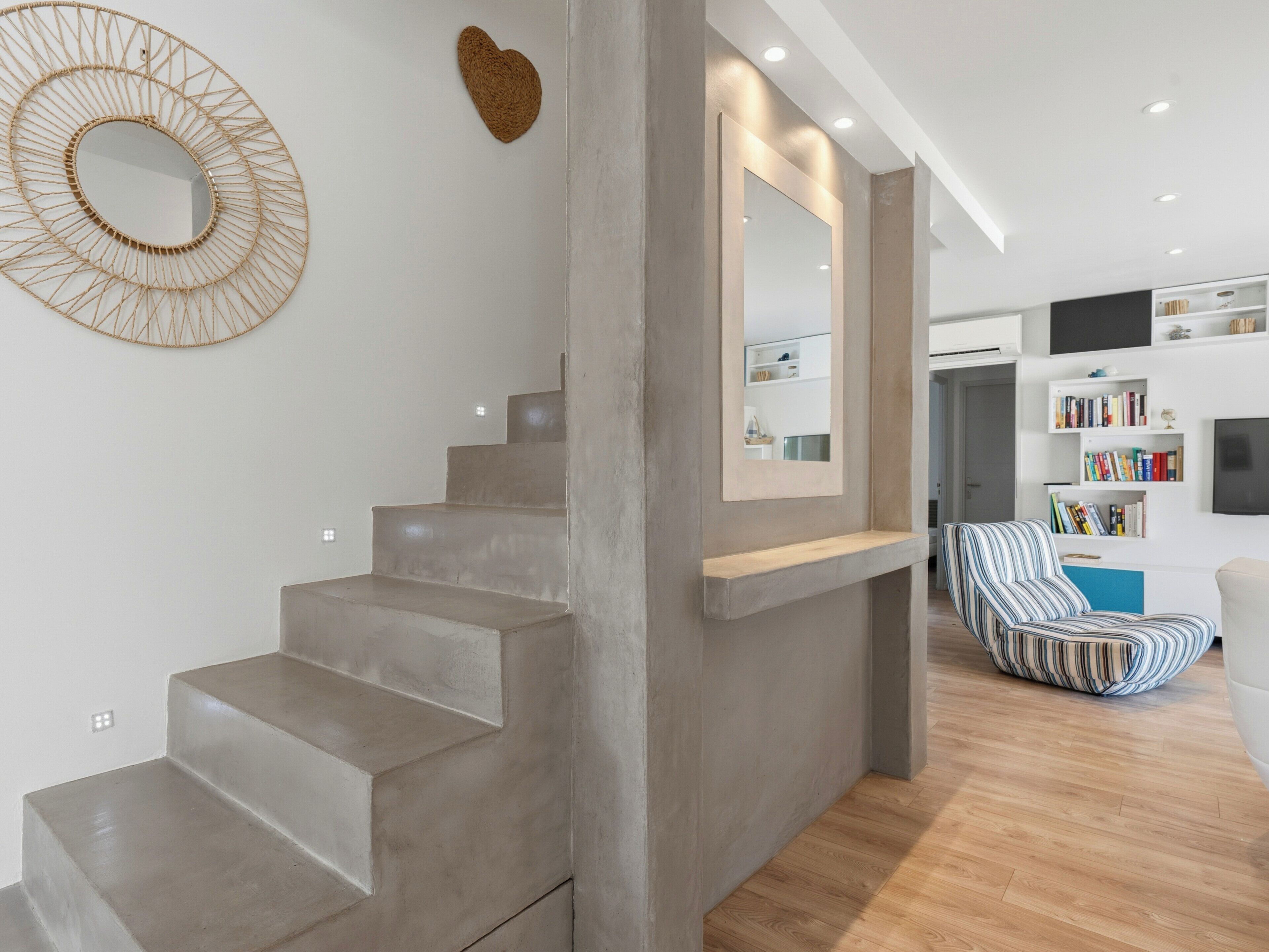 Een modern interieur met een betonnen trap, een decoratie in de vorm van een hart, een grote spiegel en een gestreepte stoel.