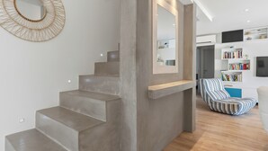 A modern interior with a concrete staircase, a heart-shaped wall decoration, a large mirror, and a striped chair.