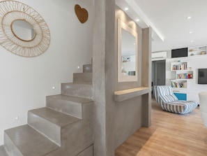 Un intérieur moderne avec un escalier en béton, un élément décoratif mural en forme de cœur, un grand miroir et une chaise à rayures.