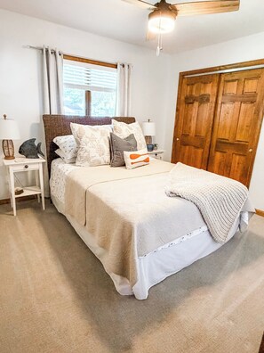 Een slaapkamer met een bed, nachtkastjes, een houten deur en een plafondventilator.