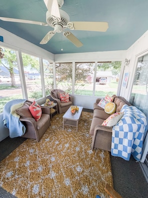 A sunroom with a ceiling fan, wicker furniture, and a view of the outdoors.