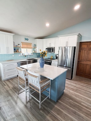 A kitchen with white cabinets, a central island, a microwave, a refrigerator, and a wooden floor.