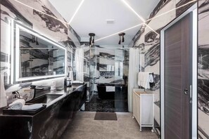Un baño moderno con un espejo grande, una bañera negra y un box de ducha de vidrio.
