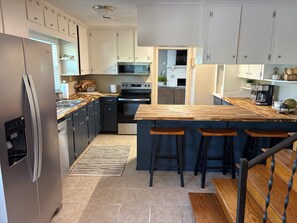 Una cocina moderna con un refrigerador de acero inoxidable, un horno empotrado, un microondas y una isla de madera con taburetes de bar.