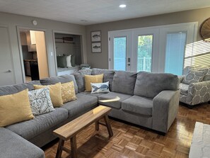 Una sala de estar con un sofá seccional gris, un banco de madera y cojines estampados.