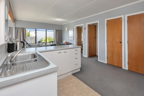 Eine moderne Küche mit einer großen Kochinsel, einem Spülbecken und einem Essbereich mit Stühlen. Holzfenster und Blick ins Grüne.