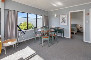 Ein Zimmer mit Esstisch, Stühlen, einem Teleskop, einer gerahmten Illustration von Fischen und einem Bett im Hintergrund.