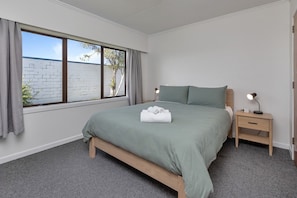 Ein Schlafzimmer mit einem Bett, einem Nachttisch, einer Lampe und einem Fenster mit Vorhängen.