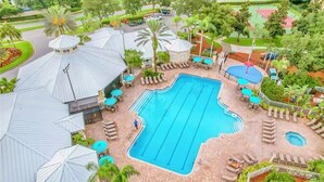A swimming pool with lounge chairs and umbrellas, surrounded by palm trees and a covered area with a roof. - Cozy 3-bedroom townhome with AC in perfect Kissimmee (Kissimmee)