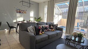 A modern living room with a grey sofa, a coffee table, and a dining area with a table and chairs. - Cozy 3-bedroom townhome with AC in perfect Kissimmee (Kissimmee)