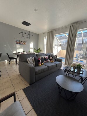 Ein modernes Wohnzimmer mit grauem Sofa, einem Couchtisch und einem Essbereich mit Tisch und Stühlen.