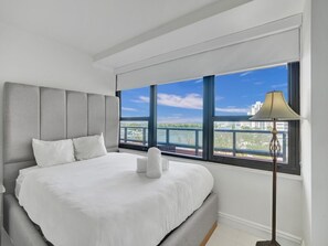 Ein modernes Hotelzimmer mit einem großen Bett, Blick auf die Stadt und einer Stehlampe.