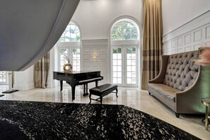 Ein großzügiger Raum mit einem Klavier, einer Couch und einem großen Fenster mit Vorhängen.