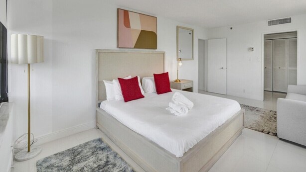 Una habitación de hotel con una cama grande, una mesita de noche, una lámpara, un espejo y un armario.