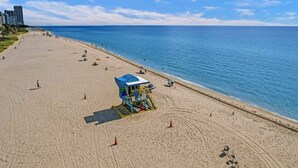 Una playa con un puesto de salvavidas, cielo azul despejado y mar tranquilo.