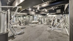 Un gimnasio con diversos equipos de ejercicio, como máquinas de pesas y mancuernas, dispuestos sobre un piso alfombrado.