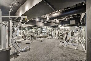 Ein Fitnessraum mit verschiedenen Trainingsgeräten, darunter Kraftgeräte und Kurzhanteln, auf einem Teppichboden.