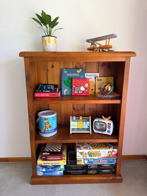 Ein Holzregal mit verschiedenen Kinderbüchern, einem Spielzeugflugzeug und einem Blumentopf.