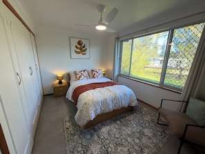 Ein Schlafzimmer mit Bett, Nachttisch, Deckenventilator, Fenster mit Blick und einer Tür.