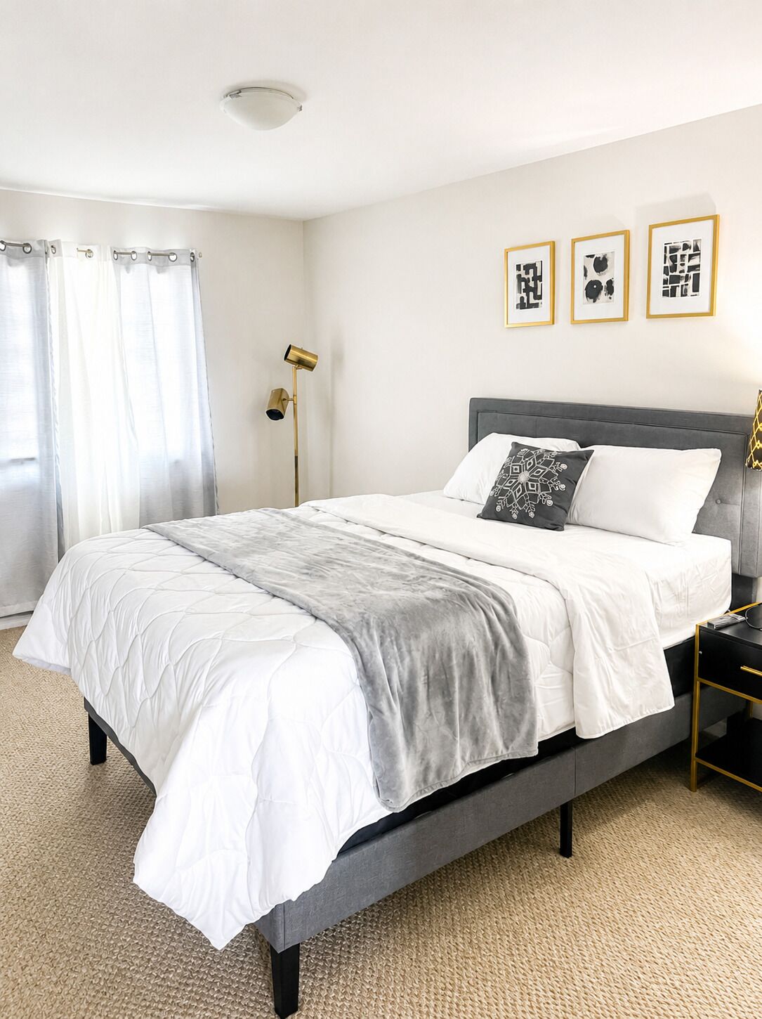 A modern bedroom with a bed, curtains, a floor lamp, and three framed pictures on the wall.