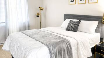 A modern bedroom with a bed, curtains, a floor lamp, and three framed pictures on the wall.