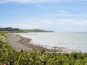 Et kystlandskab med en stenet kystlinje, en moler, der strækker sig ud i vandet, og en grøn bakke i det fjerne.