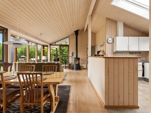 Ein modernes Interieur mit einer Holzessecke, einer Küche mit weißen Schränken und einem großen Fenster mit Blick auf Grünflächen.