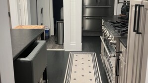 Ett kök med vita skåp, rostfria vitvaror, en svart bänkskiva och en mönstrad matta.
