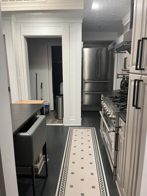 Una cocina con armarios blancos, electrodomésticos de acero inoxidable, encimera negra y alfombra estampada.