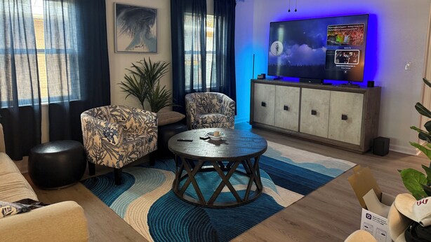 Een woonkamer met een bank, fauteuil, rond bijzettafeltje en een televisie op een dressoir.