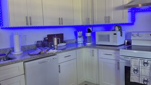 Een moderne keuken met witte kasten, een magnetron, een koffiezetapparaat en een fornuis.