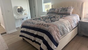 Een slaapkamer met een bed, nachtkastje, kaptafel, spiegel en raam.