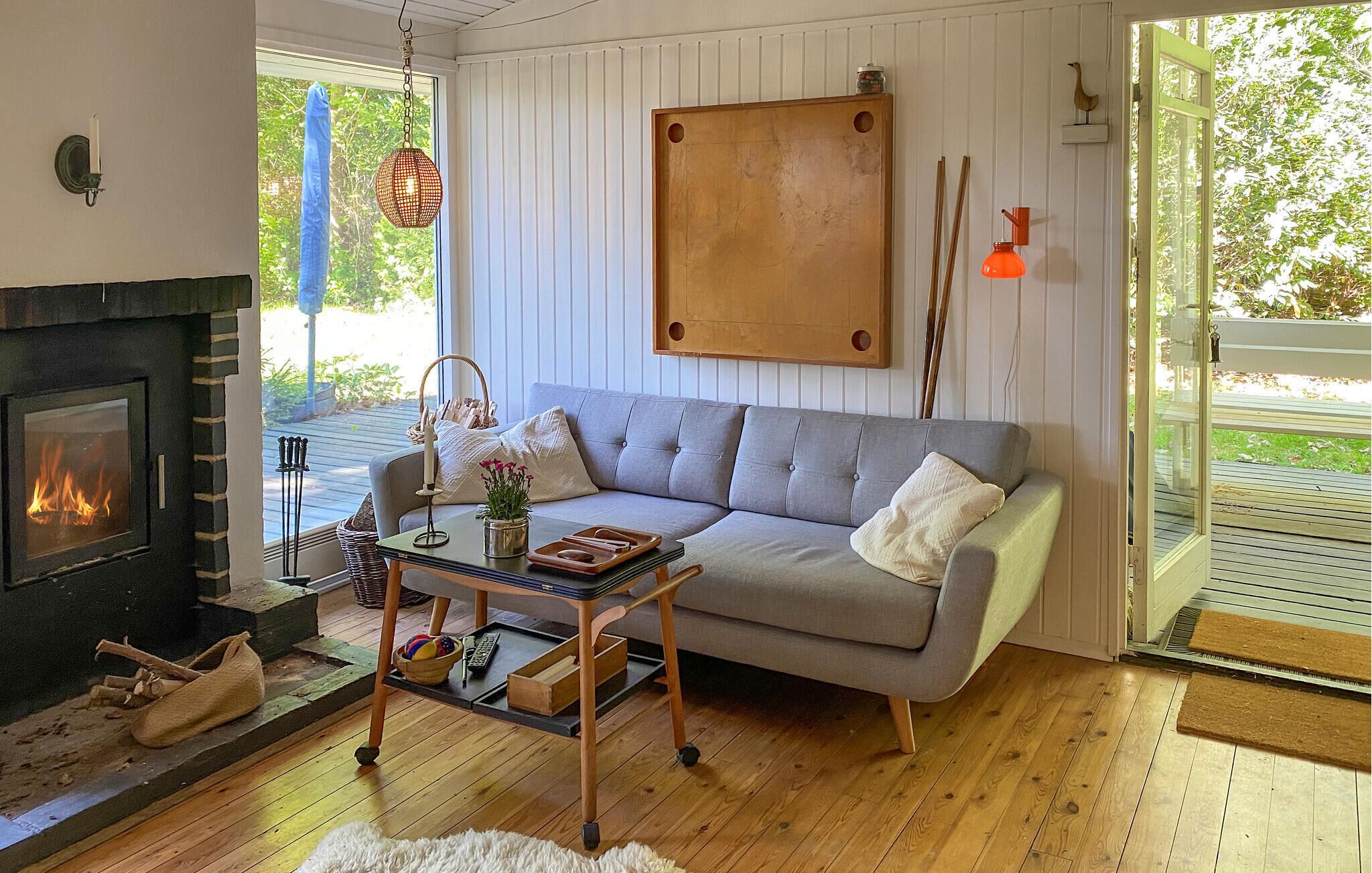 Una sala de estar con chimenea, un sofá gris, una mesa de centro y vistas al exterior con vegetación.