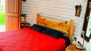 Une pièce chaleureuse avec un lit en bois, une couvre-lit rouge à motifs, une tête de lit en bois, une petite table de chevet en bois et un mur au style rustique.