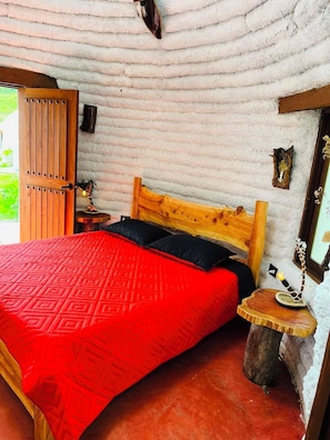 Una stanza accogliente con un letto in legno, una coperta a letto rossa con motivo, una testiera in legno, un comodino in legno e una parete rustica.