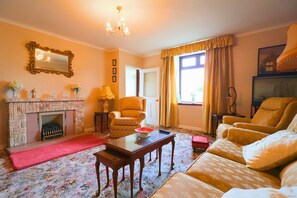 A living room with a fireplace, a sofa, a chair, and a table. - At entrance of Tollymore Park! Family sized house with large garden and parking (Newcastle)