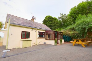 A single-story building with a sloped roof, a small porch, and a picnic table. - At entrance of Tollymore Park! Family sized house with large garden and parking (Newcastle)