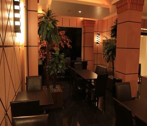 A dimly lit indoor space with a dining table, chairs, and potted plants.