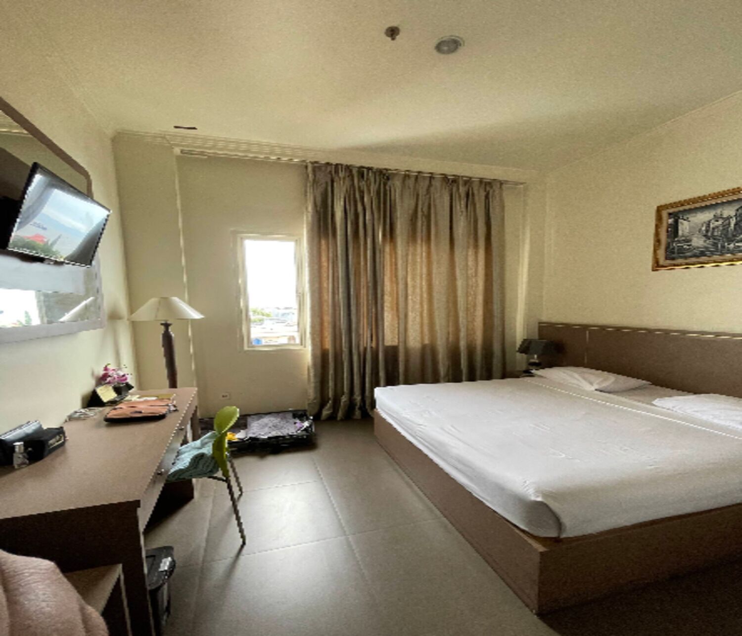A hotel room with a bed, a desk with a lamp, a television, and a window with curtains.