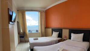 Ett hotellrum med två sängar, en tv, ett fönster med gardiner och utsikt över havet.