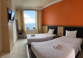Habitación de hotel con dos camas, televisión, ventana con cortinas y vista al mar.