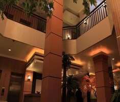 Un vestíbulo de hotel de varios niveles con una columna central, una escalera y una planta decorativa.