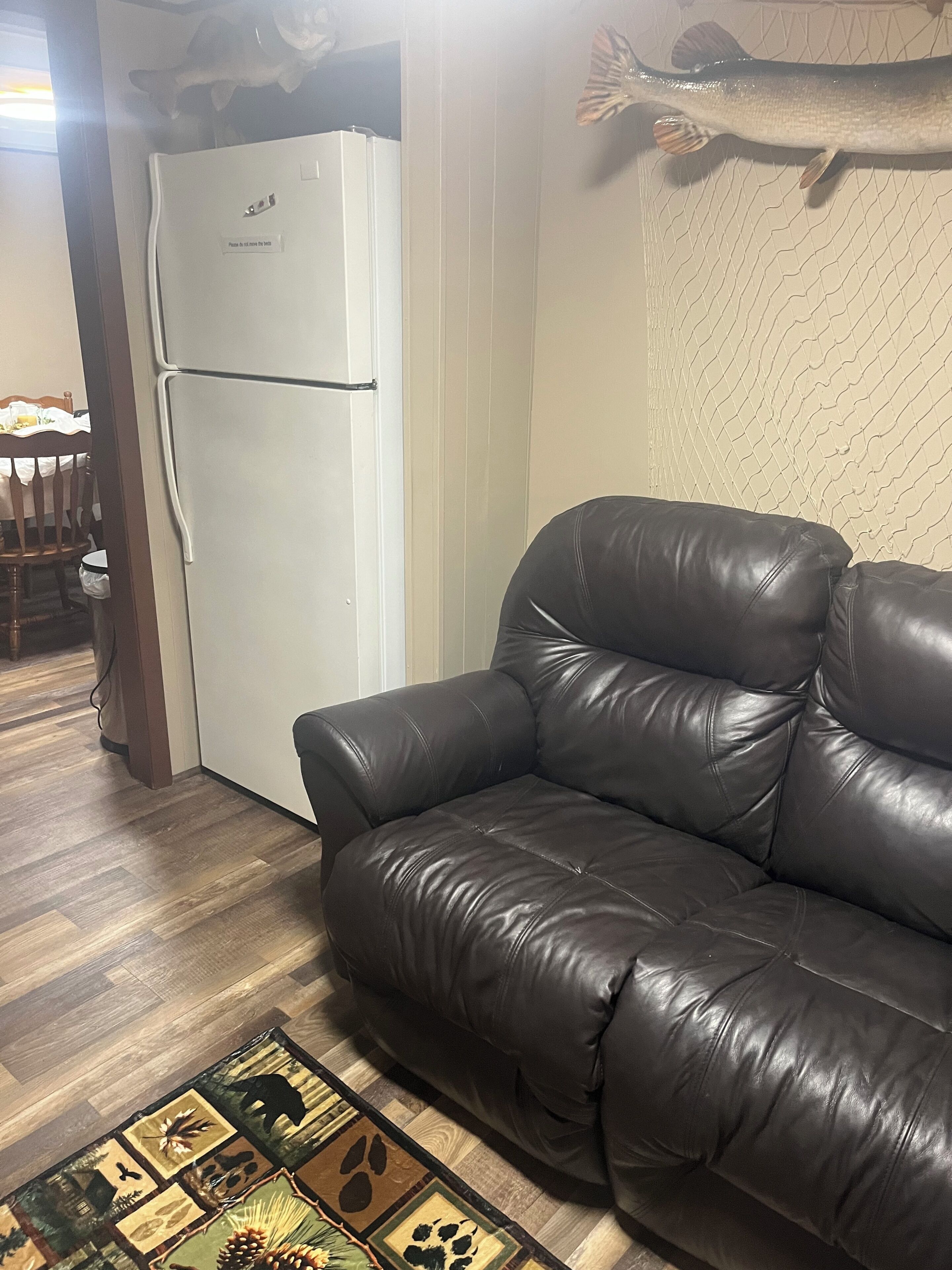 Una sala de estar con un sofá de cuero negro, un refrigerador blanco y un tapete estampado.