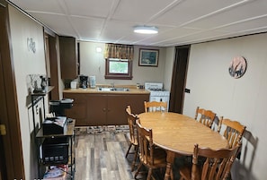 Ein Essbereich mit Holztisch und -stühlen, eine Küche mit Herd und Spüle sowie eine Uhr an der Wand.