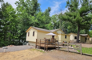 A yellow cabin with a wooden deck, a table with chairs, and a covered area with an umbrella.