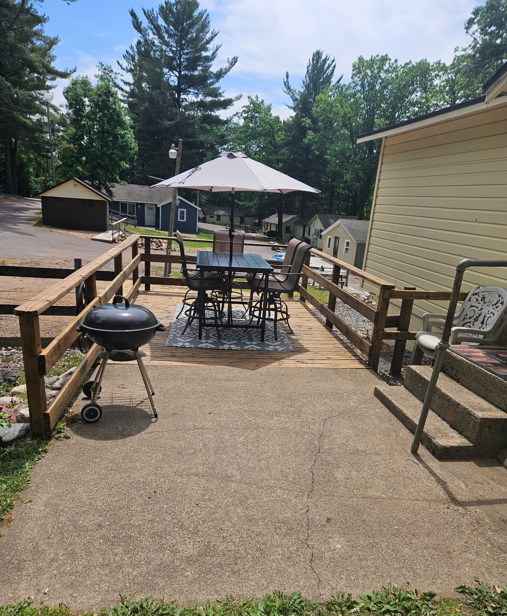 A patio with a grill, table, chairs, and an umbrella.
