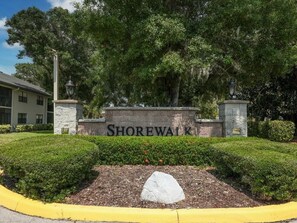 A sign with 'SHOREWALK' in front of a building, surrounded by greenery and a yellow curb.