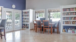 Ein Zimmer mit Esstisch, Stühlen, Deckenventilator, Bücherregal und einer Wanduhr.